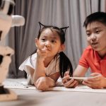Adaptive Cellular Robotics for Autonomous Infrastructure Two children interact with a robotic toy while using a smartphone, showcasing modern technology indoors.
