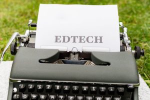 A vintage typewriter displays 'EdTech' on paper, set outdoors on grass.