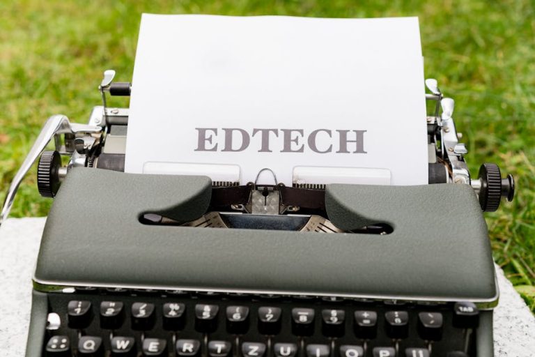 A vintage typewriter displays 'EdTech' on paper, set outdoors on grass.