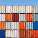 Colorful stacked shipping containers against a vibrant blue sky, conveying global trade and logistics.