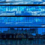 Architecting Cloud-Native Neurosymbolic Systems for Neuroethics Modern glass building reflecting urban skyline and blue sky with clouds.
