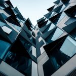 Architecting Resilience: A Provably-Safe Topological Standard A low-angle view of futuristic modern architecture featuring unique geometric patterns and glass facade.