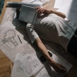 Self-Healing Neurosymbolic AI for Synthetic Media A man in casual attire resting on floor with architectural drawings and notebook.