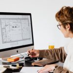 Architectural Intelligence: Designing Environments for High Performance Side view of anonymous female employee in casual clothes and eyeglasses writing out information from computer while working at table in modern light office