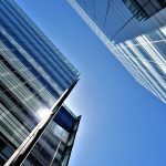 Architecture and Environment: The Strategic Legacy of Built Spaces Low angle view of glass skyscrapers reflecting the bright sun in a clear blue sky.