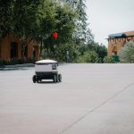 A futuristic autonomous delivery robot moving on an empty city street.