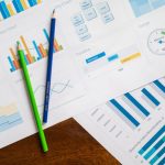 Flat lay of various business charts and colored pencils on wooden table, highlighting financial analysis.