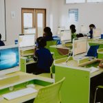 Children learning in a modern computer lab environment with headphones and desktops.