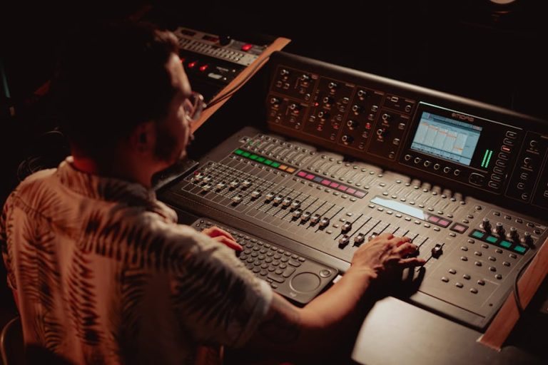 Audio engineer adjusts controls on professional mixing console in a dimly lit recording studio.