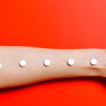 Conceptual image of an arm with pills lined up, set against a vivid red background, symbolizing healthcare themes.