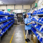 Bio-Inspired Supply Chain Resilience: Self-Healing Logic Woman in uniform organizing inventory in a warehouse aisle with labeled bins.