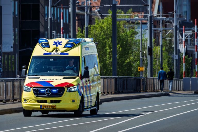 A bright yellow ambulance drives on a city street during daytime, showcasing emergency services in action.