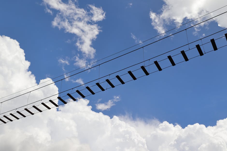 A low angle view of a suspended footbridge set against a vibrant blue sky and clouds.