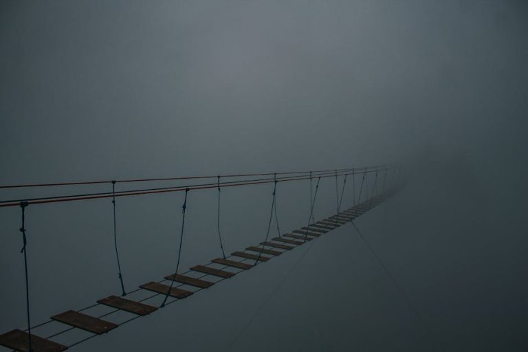 Spooky suspension bridge vanishing into a dense fog, creating a mysterious atmosphere.