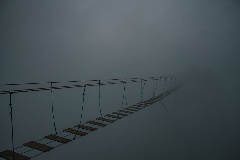 Spooky suspension bridge vanishing into a dense fog, creating a mysterious atmosphere.