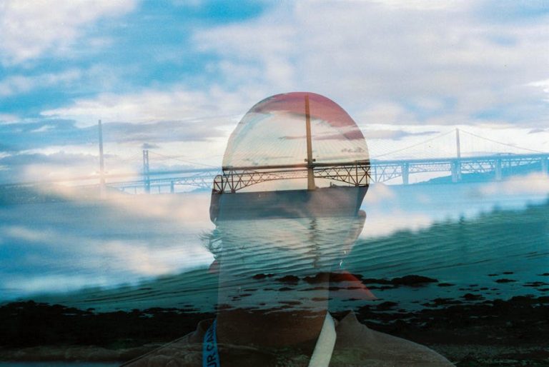 A surreal double exposure of a man and a bridge with a dreamy sky backdrop.