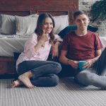 Building a Causal Inference Compiler for Resilient Supply Chains Casual couple sitting on bedroom floor, smiling at camera setup.