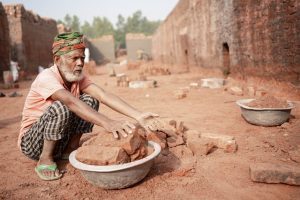 An elderly man works sorting bricks in a rural brick field in Dhaka Division, Bangladesh, illustrating hard labor and resilience.