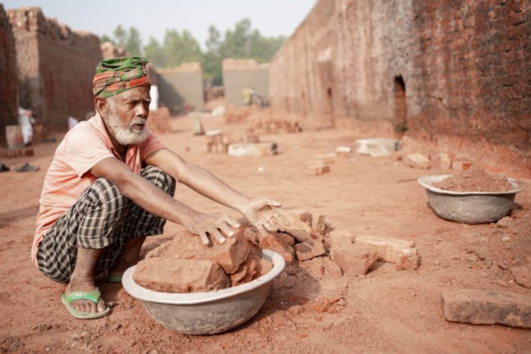 An elderly man works sorting bricks in a rural brick field in Dhaka Division, Bangladesh, illustrating hard labor and resilience.