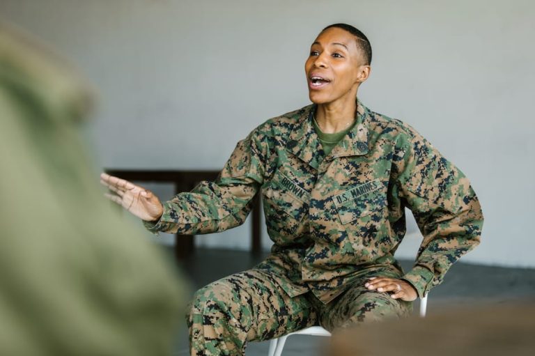 Female veteran in U.S. Marine Corps uniform smiling and gesturing during a discussion indoors.
