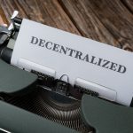 Close-up of a vintage typewriter printing 'DECENTRALIZED' on paper over wooden surface.