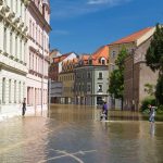 <h1>Building Urban Resilience: The Role of Risk-Sensitive Supply Chain Simulators</h1> People navigating a flooded street in a European town on a sunny day.