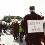 Participants at a climate rally gather on a cobblestone street with signs advocating for the future.
