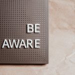 Secure Economic Policy Analysis With Causality-Aware SMPC Be Aware wording on brown textured perforated surface, offering copyspace.