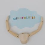 Wooden mannequin arms holding a blue cloud with 'Mindfulness' text, promoting self-awareness.