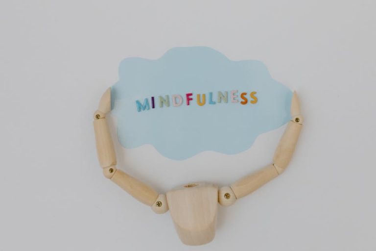 Wooden mannequin arms holding a blue cloud with 'Mindfulness' text, promoting self-awareness.