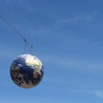 Causality-Aware tinyML for Planetary Geoengineering A realistic globe hanging on cables against a vivid blue sky, representing global unity.