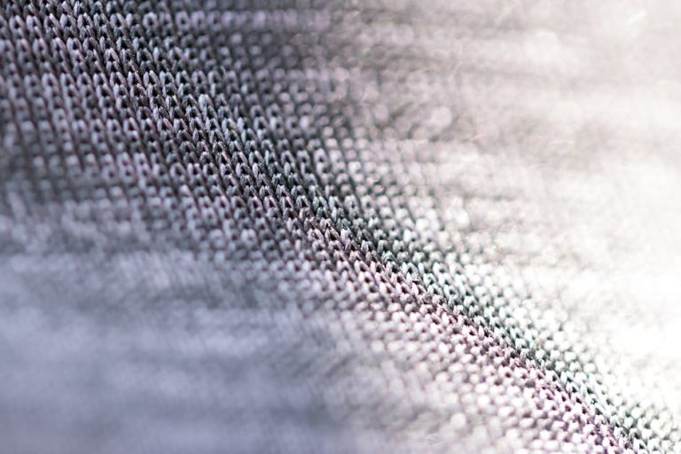 Closeup of fragment of abstract fabric sewn from thin grey threads against blurred background