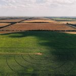 Stunning aerial view of a green circular field surrounded by rural landscape with crop fields.