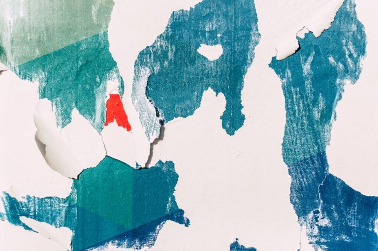 A close-up of a textured wall with layers of colorful peeling paint, creating an abstract pattern.