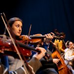 <h1>Competitive Edge Orchestration: Mastering Control Policies for AR/VR/XR Environments</h1> A group of musicians perform in an orchestra, featuring a violinist in focus.