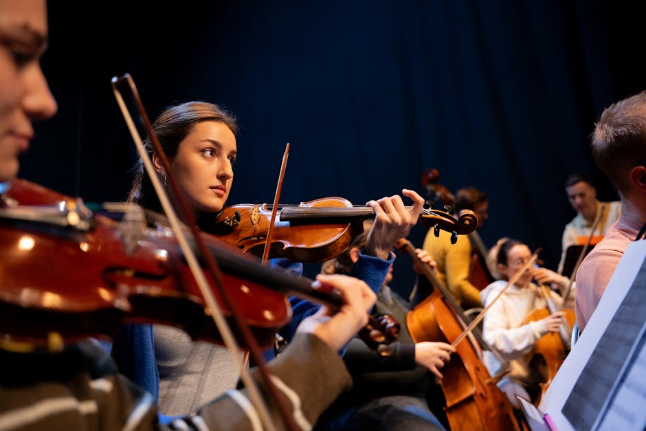 A group of musicians perform in an orchestra, featuring a violinist in focus.