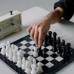 Hand makes a chess move with a classic chess clock, highlighting strategy and focus.