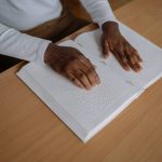 <h1>Continual-Learning Adaptive Autonomy: The Future of Intelligent Healthcare Systems</h1> Hands reading a braille book on a wooden table, emphasizing tactile learning and accessibility.