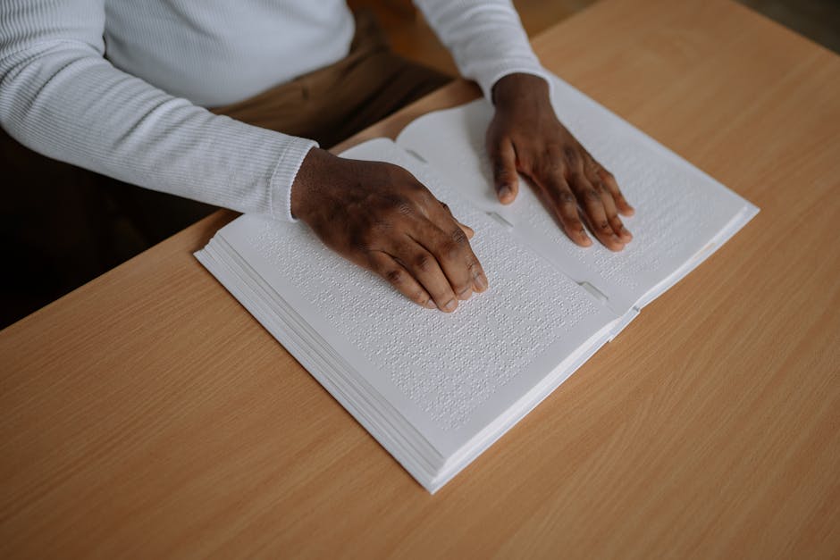 Hands reading a braille book on a wooden table, emphasizing tactile learning and accessibility.