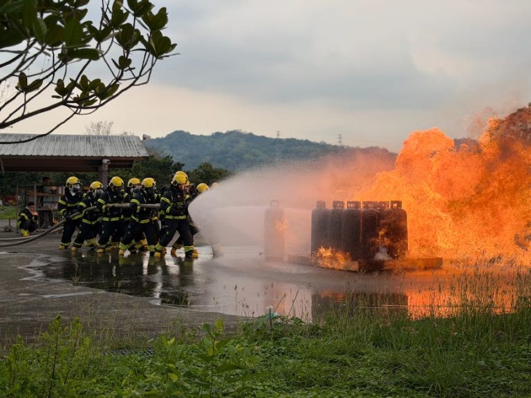 Team of firefighters using hoses to extinguish a controlled outdoor blaze during training.