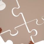 Cooperative Alignment: The Future of Value-Aligned Robotics Hands of diverse individuals holding large puzzle pieces, symbolizing teamwork and unity.