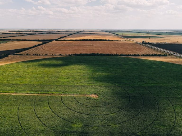 Stunning aerial view of a green circular field surrounded by rural landscape with crop fields.