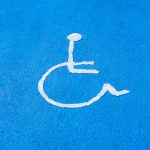Clear blue disabled parking sign on asphalt surface, symbolizing accessibility.