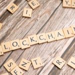 Wooden letter tiles form the word 'blockchain' arranged on a rustic wood background.
