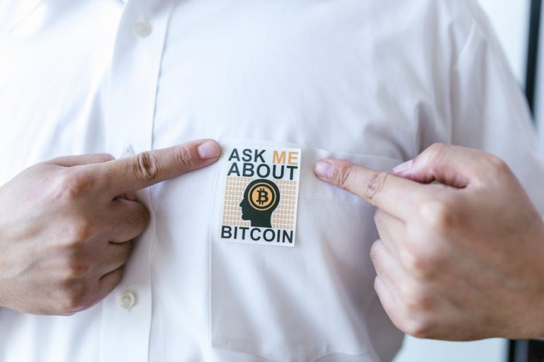 Close-up of a person pointing at a Bitcoin awareness sticker on a shirt.