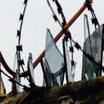 Close-up view of rusted barbed wire with jagged broken glass, conveying danger and security.