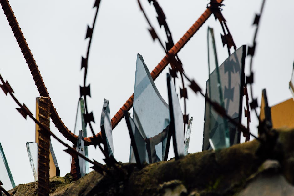 Close-up view of rusted barbed wire with jagged broken glass, conveying danger and security.