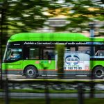 A green natural gas bus in motion on a city street, emphasizing eco-friendly transportation.