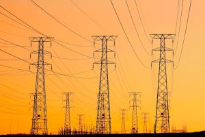 Silhouetted power lines against a vibrant orange sunset, symbolizing energy and infrastructure.