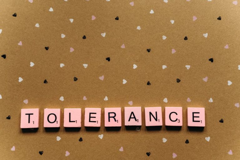 Scrabble tiles spelling 'tolerance' on a heart-patterned background, promoting acceptance.